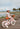 Fillette de 3 ans portant un casque rose Bebikeen à côté de son vélo 12 pouces rose avec panier en osier et roues stabilisatrices, au bord de la mer.