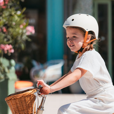 Fille portant le casque vélo enfant BeBikeen XS crème, 2 à 6 ans, sur vélo 16 pouces crème, vue de profil gauche.