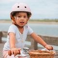 Fillette portant le casque vélo enfant Bebikeen XS rose, conçu pour les enfants de 2 à 6 ans, assise sur son vélo avec panier en osier en bord de mer.