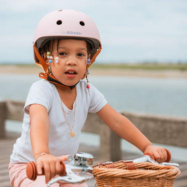 Fillette portant le casque vélo enfant Bebikeen XS rose, conçu pour les enfants de 2 à 6 ans, assise sur son vélo avec panier en osier en bord de mer.