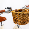 Détail du vélo enfant Bebikeen avec panier en osier naturel et attaches en simili cuir marron, poignées de freins chromées et jolie sonnette chromée.