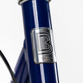 Macaron métallique BeBikeen apposé sur le cadre bleu marine, signature d’un design soigné et d’une fabrication pensée pour durer.