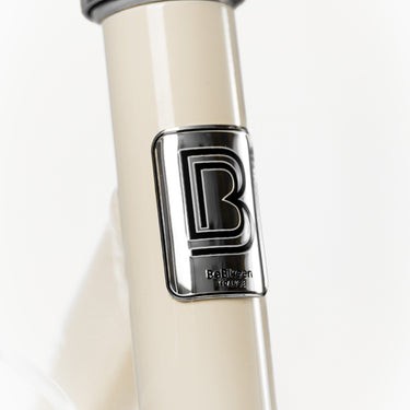 Macaron métallique de la marque française BeBikeen apposé sur le cadre crème intemporel, signature d’un design soigné et d’une fabrication pensée pour durer.