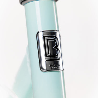 Macaron métallique de la marque française BeBikeen apposé sur le cadre bleu turquoise lumineux, signature d’un design soigné et d’une fabrication pensée pour durer.