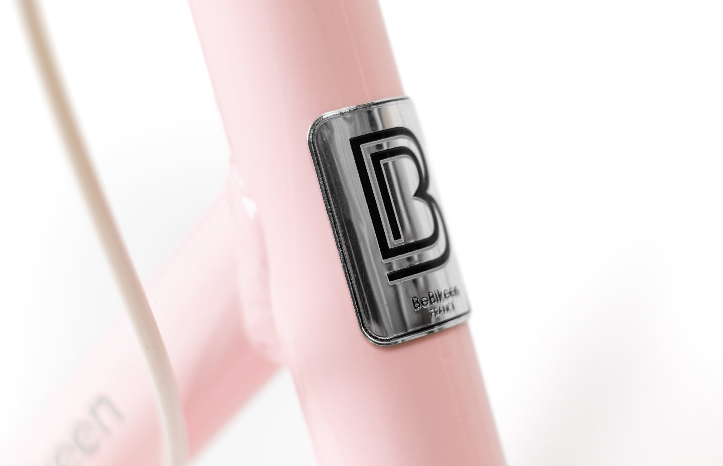 Détail du logo Bebikeen. Macaron métallique sur le cadre d’un vélo enfant rose, détail de la marque française BeBikeen "L’allure parfaite".