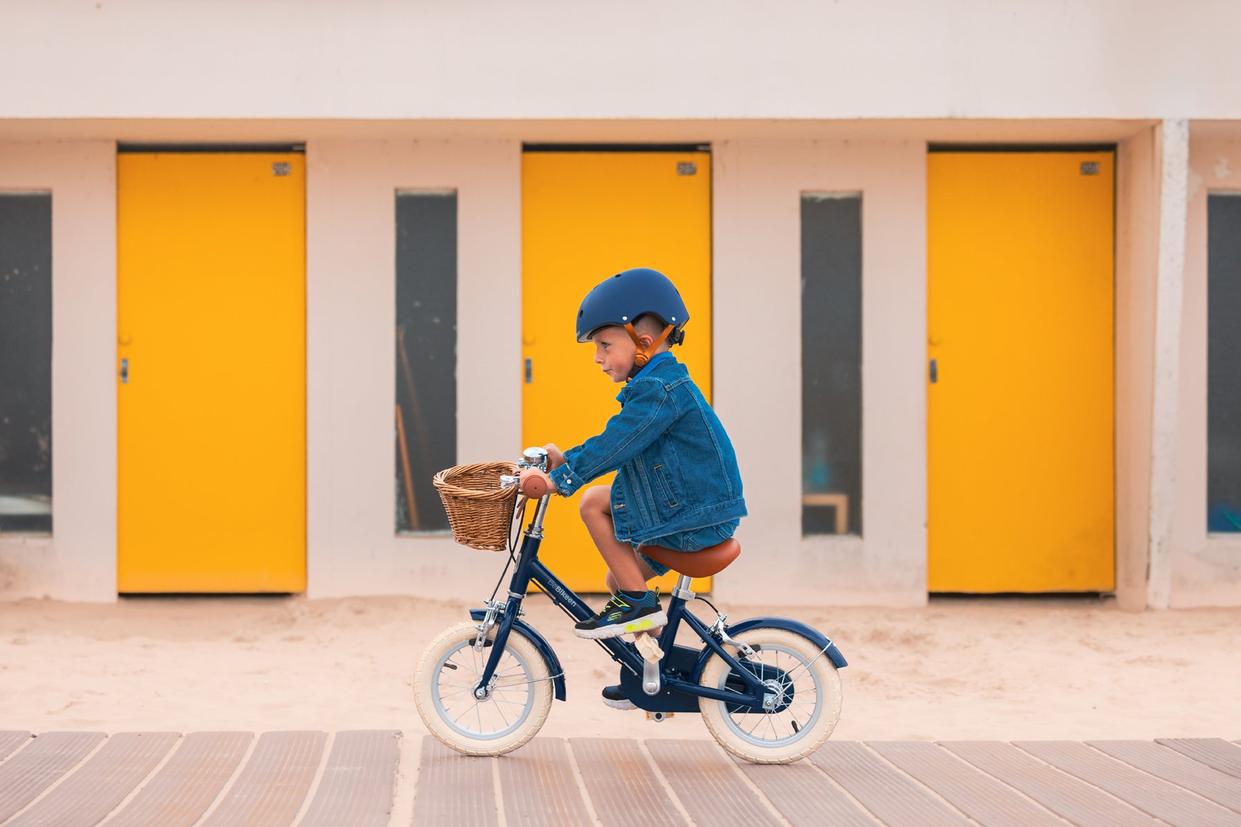 Garçon pédalant sur son vélo léger Bebikeen 12 pouces bleu marine avec panier en osier, photo prise au Touquet.
