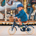 Garçon de 3 ans roule avec aisance sur le vélo léger Bebikeen 12 pouces bleu marine, 2 à 4 ans, sur une place du Touquet devant un manège.