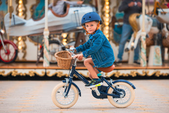 Garçon de 3 ans roule avec aisance sur le vélo léger Bebikeen 12 pouces bleu marine, 2 à 4 ans, sur une place du Touquet devant un manège.