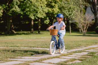 Garçon de 6 ans pédale sur son vélo Bebikeen 16 pouces bleu marine, équipé d’un panier en osier. L'enfant porte un casque assorti.