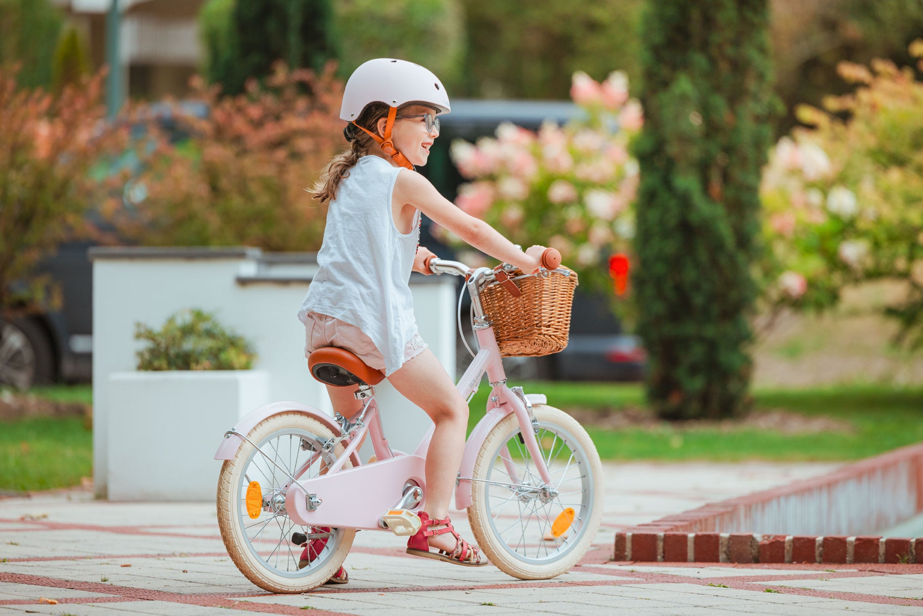 Fillette de 6 ans ans souriante, portant un casque rose, pédale sur son vélo Bebikeen 16 pouces rose avec panier en osier au Touquet.