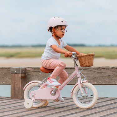 Fillette de 3 ans roule sur le vélo enfant Bebikeen 12 pouces rose, léger, 2 à 4 ans, vue de profil avec roues stabilisatrices.