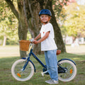 Garçon 5  ans à côté de son vélo léger Bebikeen 16 pouces bleu marine, équipé d’une béquille et d’une selle marron en simili cuir.
