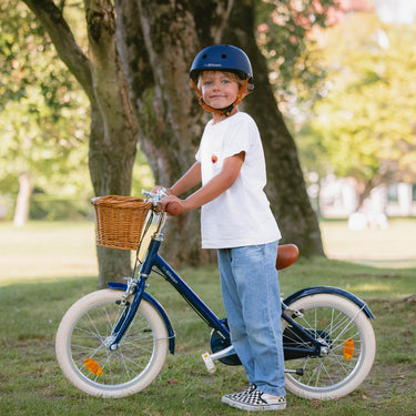 Garçon 5  ans à côté de son vélo léger Bebikeen 16 pouces bleu marine, équipé d’une béquille et d’une selle marron en simili cuir.