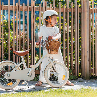 Fille de 5 ans à côté de son vélo enfant Bebikeen 16 pouces crème léger, 4 à 6 ans, avec béquille et selle marron en simili cuir.