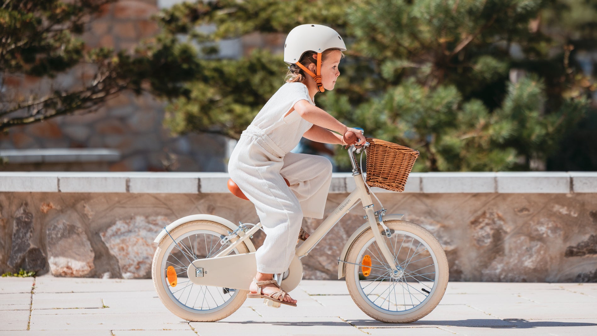 Fille de 5 ans pédale sur vélo Bebikeen 16 pouces crème léger avec panier en osier, casque crème assorti pour la protéger.