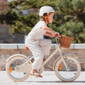 Fille de 5 ans pédale sur vélo Bebikeen 16 pouces crème léger avec panier en osier, casque crème assorti pour la protéger.