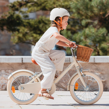 Fille de 5 ans pédale sur vélo Bebikeen 16 pouces crème léger avec panier en osier, casque crème assorti pour la protéger.