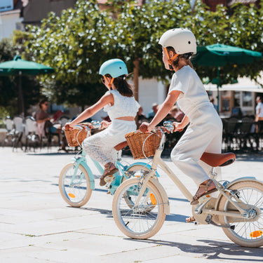 Fille de 5 ans pédale sur vélo enfant Bebikeen 16 pouces crème léger, avec selle marron en simili cuir et panier en osier naturel.