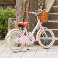 Vélo léger enfant Bebikeen 16 pouces rose, 4 à 6 ans, posé sur sa béquille avec panier en osier naturel et selle marron en simili cuir