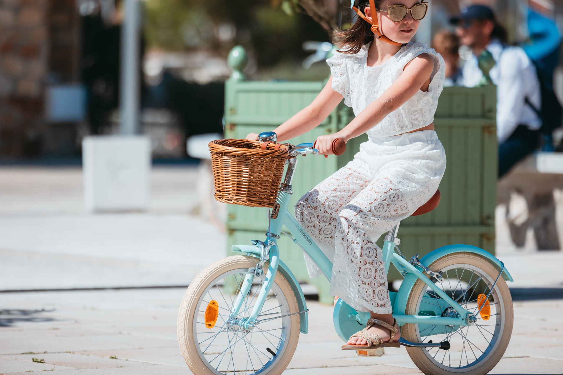 Fillette élégante en tenue blanche pédale sur son beau vélo Bebikeen 16 pouces bleu turquoise avec panier en osier.