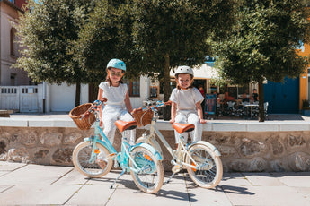 Deux filles assises à côté de leurs vélos Bebikeen 16 pouces bleu turquoise et crème, équipés de béquilles et de paniers en osier.