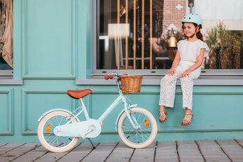 Fille assise à côté de son vélo Bebikeen 16 pouces bleu turquoise, pour enfant de 4 à 6 ans, équipé d’une béquille et d’un panier en osier.
